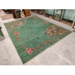 Large Early hand woven rug with flower design set on a green background. 12 ft by 9ft.