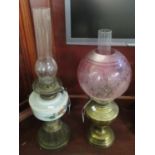 Two early 20th Century double oil lamps; one with globular cranberry etched foliate shade, the other