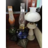Three early 20th Century oil lamps with green and blue glass reservoirs, one on an opaline glass