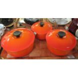 Three Le Creuset saucepans with lids in orange glaze with turned wooden handles. (B.P. 21% + VAT)