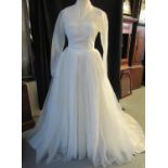 Layered net wedding dress with fitted bodice, translucent net shoulders and sleeves and pleated