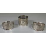 Pair of white metal napkin rings marked H & M, together with another engine turned napkin ring. (
