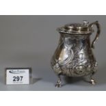Victorian silver mustard pot repousse decorated with flowers and foliage on three hoof feet. With