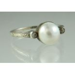 An early 20th century pearl and diamond ring set in engraved white metal with an engraved band. Ring