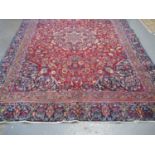 Large Middle Eastern design carpet on a red and blue ground with central floral and foliate