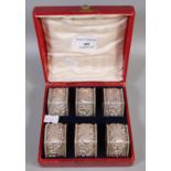 Cased set of six silver repousse decorated octagonal napkin rings with 'C' scroll and flowerhead