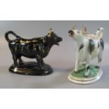 Two 19th century pottery cow creamers, one black and white the other with black and gilt lustre