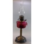 Early 20th century double burner oil lamp, having cranberry glass reservoir on a brass and