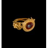 A GOLD & GARNET GEMSTONE RING SET WITH EROS EITHER SIDE, ROMAN OR LATER 2ND CENTURY A.D.