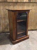 An Edwardian music cabinet with moulded canted top above a glazed door enclosing a shelved interior,