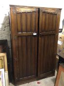 An oak wardrobe with dentil cornice above a pair of inset panel doors enclosing a plain interior, on