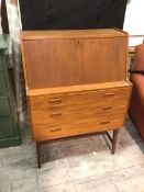 A mid century teak bureau, the slope fall front over a fitted interior, above three graduated