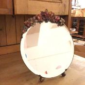 A circular dressing table mirror with carved polychrome flowers above a bevelled glass, on bun