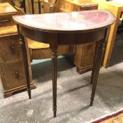 A reproduction demi lune table with glass top above a tooled leather surface on turned fluted
