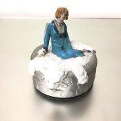 A 1920s powder puff box with seated figure on a bearskin style rug, painted with polychrome