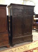 A late 19thc/early 20thc oak Tudor style wardrobe with a pair of panelled doors enclosing hanging