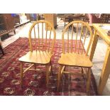 A pair of Ercol light ash spindle back kitchen chairs, with shaped saddle seats, on turned