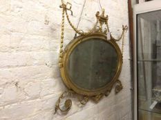 A late 19thc/early 20thc wall mirror with urn surmount and ribbon swags, oval bevelled glass