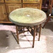 A Middle Eastern occasional table with circular brass top, with relief foliate decoration, on a