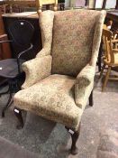 An early 20thc wing back armchair, upholstered in a hexagonal fabric with multiple stylised flowers,