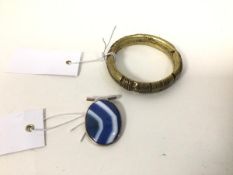 A polished oval stone pendant within a white metal mount (5cm) and a brass, possibly African, bangle