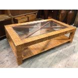 A modern coffee table, with woven cane frame and glass panel top above lower tier, on block feet (