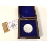 A white metal coin in presentation box along with Certificate of Precious Metal Test, issued by