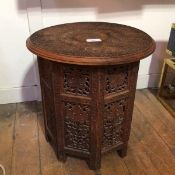A carved Indian occasional table, the circular top with a foliate design in relief above a folding