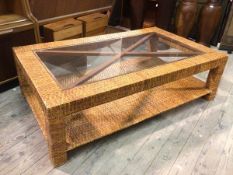 A modern coffee table with woven cane frame and glass panel top above a lower tier, on block feet (