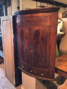 A 19thc mahogany bow front hanging corner cabinet, with two panel doors enclosing a pair of