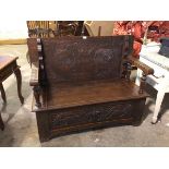 A monk's bench, the hinged top with a foliate carved decoration and moulded edge above arms with