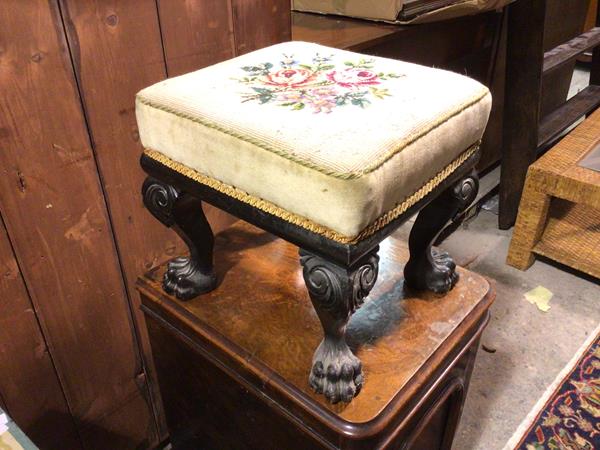 A 1920s Georgian style footstool, with ebonised base, the tapestry upholstered padded top on four