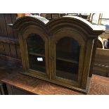 A 1920s/30s hanging cabinet, with a double arched pediment, above two glazed panel doors, with