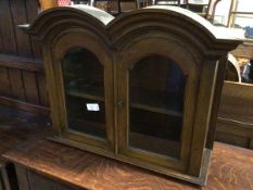 A 1920s/30s hanging cabinet, with a double arched pediment, above two glazed panel doors, with