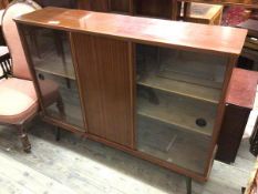 A mid century teak side cabinet, the rectangular top above two glass and one panel door, on outswept