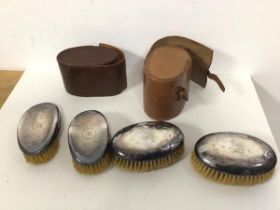 Two pairs of Edwardian hand brushes with silver backs and leather travelling cases