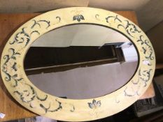 A modern wall mirror, the oval glass within a painted frame, with foliate decoration (87cm x 117cm)