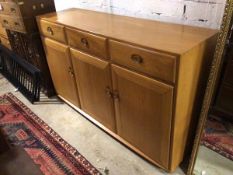 An Ercol light elm side cabinet, with three short frieze drawers above three cabinet doors, each