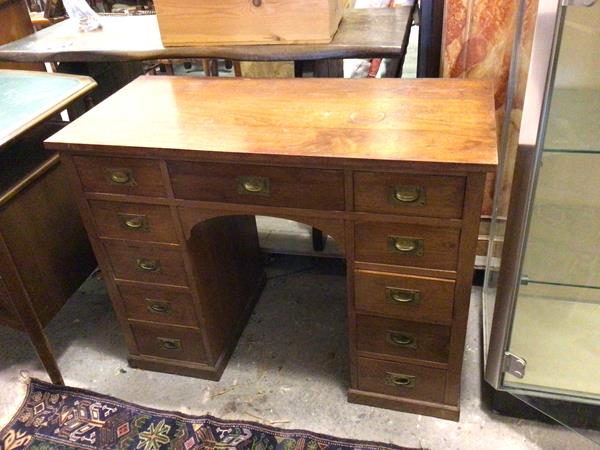 A mid 20thc campaign style desk, the rectangular top above an arrangement of drawers, with brass