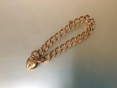 A 15ct gold curblink bracelet, suspending a 15ct gold heart padlock clasp, with safety chain. Length