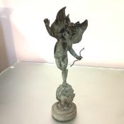 A green patinated metal figure of Cupid, mounted on a sphere, on an integral circular base. Height