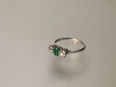 A three-stone emerald and diamond ring, the central emerald-cut emerald claw-set between a pair of