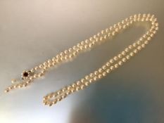 A long single strand slightly graduated cultured pearl necklace, on a 9ct gold ruby and seed-pearl