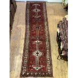 A Persian hand-knotted runner, the red ground with pole medallion, stylised bird and foliate