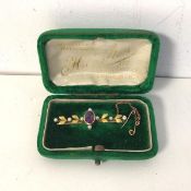 A bar brooch marked 750, with central amethyst flanked by seed pearls and leaves (4cm) (2.91g)