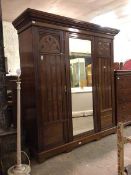 An Edwardian walnut triple wardrobe, the central mirror door enclosing an interior fitted for