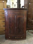 A 19thc mahogany bow front hanging corner cabinet with two panel doors enclosing a pair of shelves