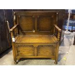 An oak monk's bench, c.1930, the panelled folding top over open arms with bobbin turned supports,