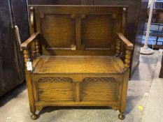 An oak monk's bench, c.1930, the panelled folding top over open arms with bobbin turned supports,