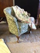 An early 20th century upholstered tub chair, with a loose fitted floral cover, raised on ball and